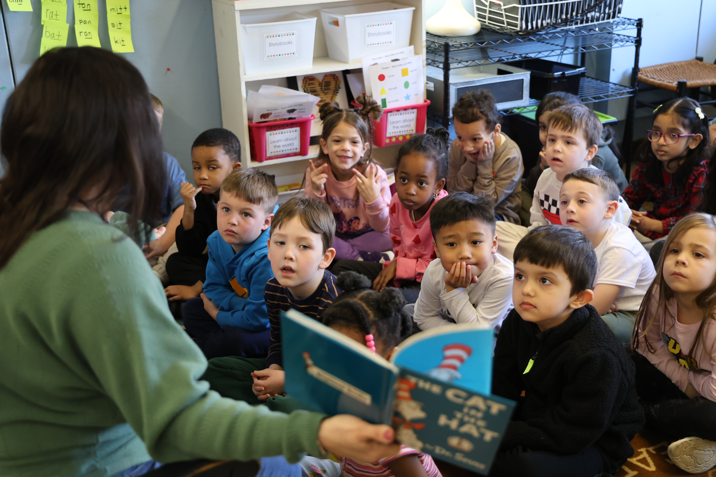 A teacher reads 'The Cat in the Hat' to a group of attentive children in a classroom.